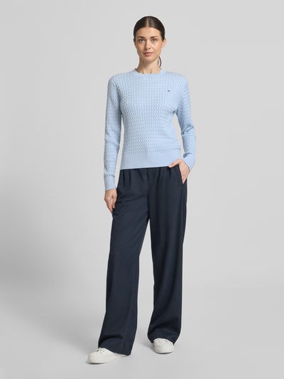 Modelka nosi Slim Fit Pullover aus reiner Baumwolle von Tommy Hilfiger, jednokolorowy sweter z okrągłym dekoltem, ścieg warkoczowy, detal z logo, imitacja dzianiny, bawełna, długi rękaw, zakończenia prążkowane, widok całej sylwetki z przodu.