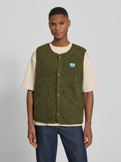 Männermodel trägt Straight Fit Weste mit Logo-Patch Modell 'Hoktown' von American Vintage in Olivgrün, Kunstfell, Ganzkörperansicht von vorne.