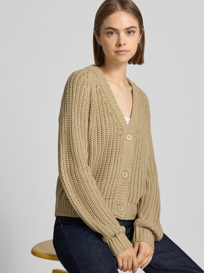 Frauenmodel trägt Relaxed Fit Cardigan in Strick-Optik Modell 'CHARLIE' von NOISY MAY®, beige, grobe Textur, Nahaufnahme Oberkörper. Rückenlänge 30 cm, Ärmellänge 70 cm, V-Ausschnitt.