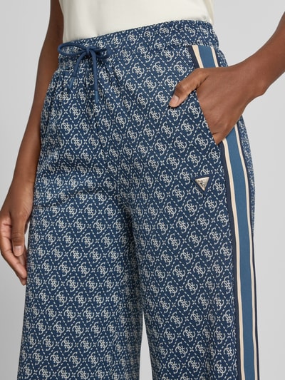 Frauenmodel trägt Sweatpants mit Logo-Muster im Allover-Look von GUESS, elastischer Bund, Tunnelzug, Wide Leg, Nahaufnahme Oberkörper.