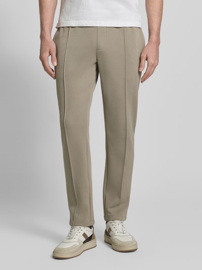 Männermodel trägt Sweatpants mit elastischem Bund von MCNEAL, Material-Mix mit Baumwoll-Anteil, lockerer Schnitt, Bundfalten, französische Eingrifftaschen, Gesäßtasche, beige Farbton, glatte Textur, Innenbeinlänge bei Größe M 75 cm, Nahaufnahme Unterkörper Vorderansicht.