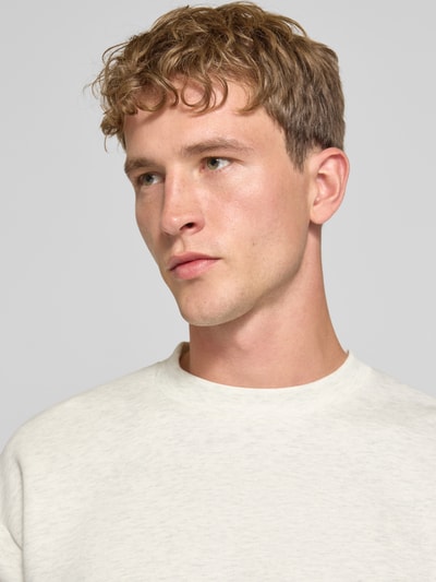 Męski model nosi Regular Fit Sweatshirt mit Baumwoll-Anteil od JACK & JONES w jasnym odcieniu, mieszanka bawełny, okrągły dekolt, krój regular fit, długi rękaw, elastyczne wykończenia, długość tyłu 65 cm, długość rękawa 59 cm, zbliżenie na górną część ciała.