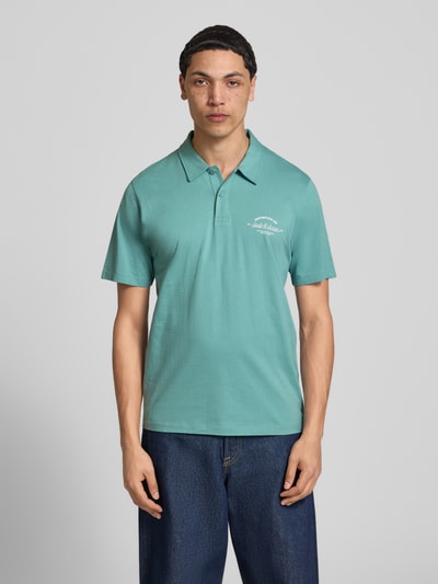 Männermodel trägt Poloshirt mit Label-Print Modell 'BRANDON' von Jack & Jones, Reine Baumwolle, Regular-Fit, Polokragen, kurze Knopfleiste, Rückenlänge 71 cm bei Größe M, Farbe türkis, glatte Textur, Ganzkörperansicht von vorne.
