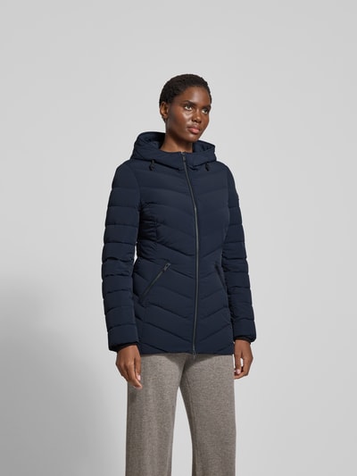 Frauenmodel trägt Daunenjacke mit Kapuze von Moose Knuckles in Dunkelblau, Material-Mix mit Stretch-Anteil, taillierter Schnitt, Reißverschluss, Reißverschlusstaschen, Rückenlänge 75 cm, Brustweite 48 cm, Ärmellänge 65 cm, Ganzkörperansicht von vorne.