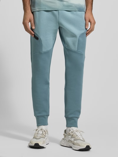 Męski model nosi Sweatpants mit Logo Modell 'Unstoppable' od Under Armour, kolor niebieski, materiał bawełniany, regular fit, widok z przodu, zbliżenie na nogi.