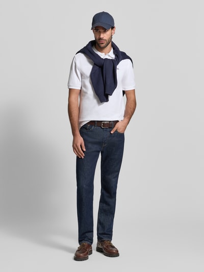 Męski model nosi Slim Fit Poloshirt mit Logo-Stitching od Gant, biała bawełna, krój slim fit, krótki rękaw, długość tyłu 70 cm w rozmiarze M, widok całej sylwetki z przodu