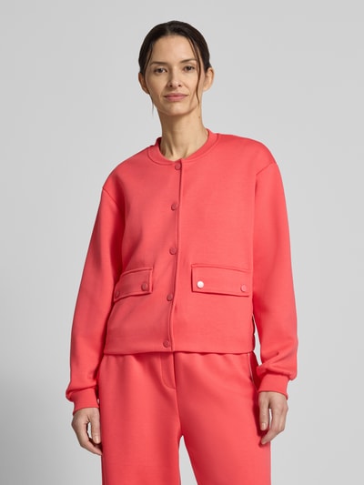 Frauenmodel trägt Regular Fit Jacke mit Viskose-Anteil Modell 'Kate' von ICHI in Koralle mit Stehkragen, Pattentaschen und Knopfleiste, Nahaufnahme Oberkörper.