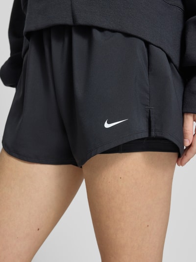 Frauenmodel trägt schwarze Damen Shorts von NIKE TRAINING im 2-in-1-Look, Modell 'One' mit Logo, Regular-Fit, Nahaufnahme Oberschenkel.