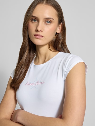 Frauenmodel trägt Slim Fit T-Shirt mit Logo-Stitching von Guess Jeans, weiß, Baumwoll-Mix, Rundhalsausschnitt, Nahaufnahme Oberkörper.