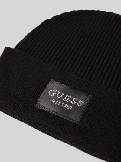 Produktfoto, schwarze Mütze aus Viskose-Mix in Strick-Optik von GUESS mit Logo-Patch und Strasssteinbesatz, Detailaufnahme.