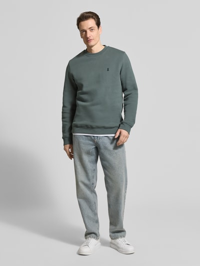 Männermodel trägt regular fit heren sweatshirt model 'BAARO FLEECE' van Armedangels, look: effen, logodetail, ronde hals, lange mouw, sweat van puur biologisch katoen, rompzoom en mouwboord geribd, grijsgroene kleur; ganzkörperansicht van voren.