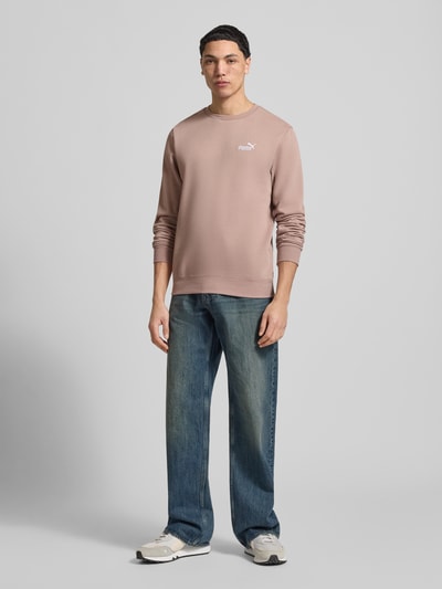 Męski model nosi Regular Fit Sweatshirt mit Logo-Stitching od PUMA PERFORMANCE, mieszanka bawełny, okrągły dekolt, elastyczne wykończenia, długość tyłu 69 cm, długość rękawów 69 cm, widok całej sylwetki z przodu.