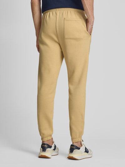 Męski model nosi Sweatpants mit elastischem Bund od GAP, beżowy bawełniany miks, krój regular fit, kieszeń z tyłu, długość nogawki wewnętrznej w rozmiarze M: 74 cm, widok całej sylwetki z tyłu.