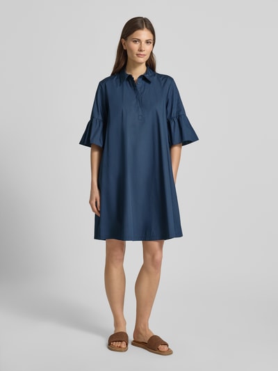 Frauenmodel trägt Knielanges Hemdblusenkleid mit Kentkragen Modell 'EPOCHE' von EMME aus reiner Baumwolle, Lockere-Schnitt, Volants, Ganzkörperansicht von vorne.