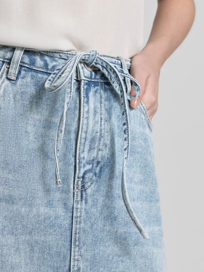 Frauenmodel trägt Midi-Jeansrock aus Baumwoll-Mix Modell 'WIEN' von Vero Moda in Denim-Optik, 5-Pocket-Design, Bindegürtel, Nieten, Nahaufnahme Oberkörper.