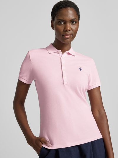 Frauenmodel trägt Slim Fit Poloshirt aus Baumwoll-Mix von Polo Ralph Lauren in zartem Rosa mit blauer Stickerei, Nahaufnahme Oberkörper. Damen Poloshirt von Polo Ralph Lauren.