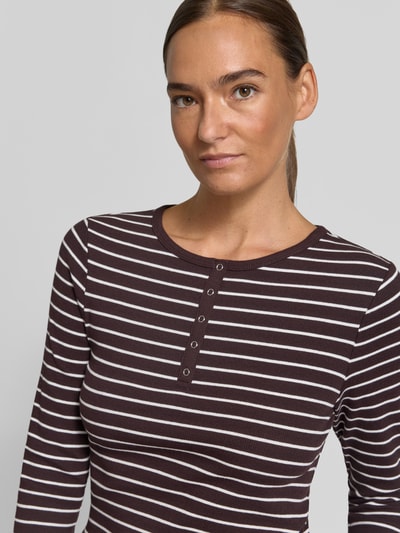 Modelka kobieca ma na sobie Slim Fit Langarmshirt aus Baumwoll-Mix mit kurzer Knopfleiste von Christian Berg Woman, elastyczny bawełniany materiał, krój slim fit, okrągły dekolt, krótka listwa guzikowa, długi rękaw, długość tyłu w rozmiarze S: 58 cm, brązowo-białe paski, tekstura prążkowana, widok z przodu, zbliżenie na górną część ciała.