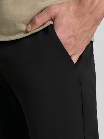 Männermodel trägt Tapered Fit Hose mit Gesäßtaschen von MCNEAL in Schwarz, glatte Textur, sichtbare Eingrifftaschen, Nahaufnahme Oberkörper. Bundweite bei Größe M: 45 cm, Innenbeinlänge bei Größe M: 80 cm, Knopf- und Reißverschluss.