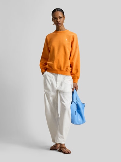 Frauenmodel trägt Oversized Sweatshirt aus Baumwoll-Mix von Polo Ralph Lauren in Orange, unifarben, Logo-Stitching, Ganzkörperansicht von vorne.