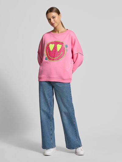 Modelka kobieca ma na sobie Oversized Sweatshirt mit Motiv-Print od miss goodlife, czysta bawełna, różowy, motywowy nadruk, luźny krój, ściągacze, okrągły dekolt, widok całej sylwetki z przodu.