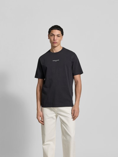 Männermodel trägt Regular Fit T-Shirt aus Baumwolle von MAISON KITSUNÉ, schwarzes Kurzarmshirt, Label-Stitching, Ganzkörperansicht von vorne.
