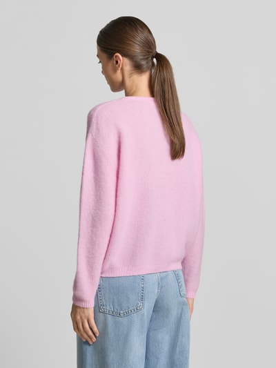 Frauenmodel trägt Strickjacke mit Woll-Anteil Modell 'VITOW' von American Vintage in Rosa, lockere Passform, Rückansicht, Ganzkörperansicht. Elastischer Material-Mix, gerippte Abschlüsse, Knopfleiste und Rundhalsausschnitt im Kontext.