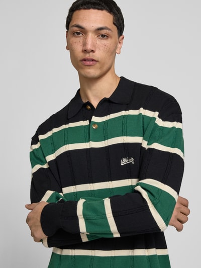 Männermodel trägt Strickpullover mit Polokragen und Label-Stitching von BLKVIS in Grün, Schwarz, Creme mit Zopfmuster, Nahaufnahme Oberkörper, Regular-Fit, Reine Baumwolle, Knopfleiste, Rückenlänge 66 cm, Ärmellänge 72 cm, Herren.