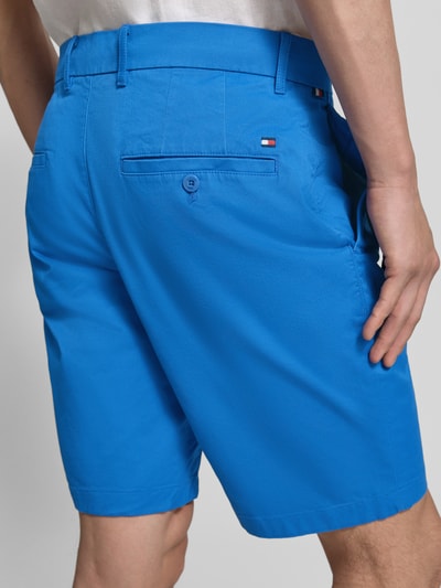 Männermodel draagt Regular Fit Bermudas aus katoenmix van Tommy Hilfiger in effen kleuren met gestikt logo en riemlussen, achteraanzicht.