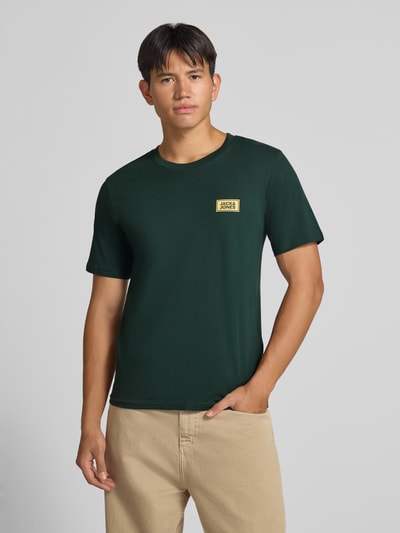 Männermodel trägt Regular Fit T-Shirt aus reiner Baumwolle mit Label-Detail von JACK & JONES, Dunkelgrün, Ganzkörperansicht von vorne. Rückenlänge bei Größe M: 67 cm, Rundhalsausschnitt.