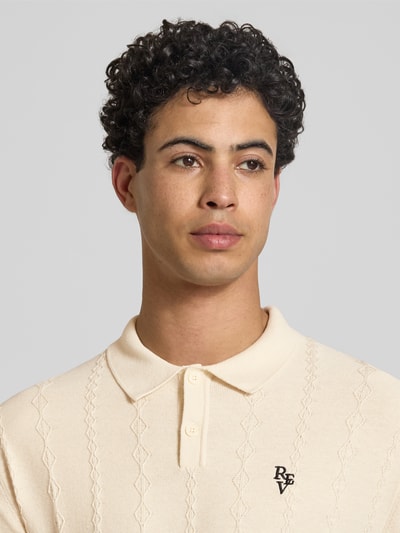 Männermodel trägt Strickpullover mit Strukturmuster und Polokragen von REVIEW aus reiner Baumwolle, Logo-Bestickung, Nahaufnahme Oberkörper.