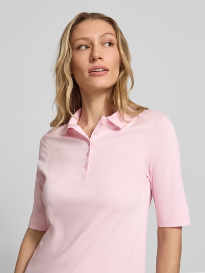 Modelka kobieca nosi Slim Fit Poloshirt mit Knopfleiste und 1/2-Arm od Christian Berg Woman, czysta bawełna, krój slim fit, różowy kolor, długość tyłu w rozmiarze 36: 61 cm, zbliżenie na górną część ciała z przodu.
