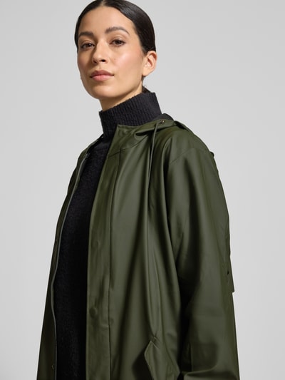 Frauenmodel trägt Regular Fit Parker mit Kapuze Modell 'Fishtail' von Rains in Olivgrün, glatte Textur, Pattentaschen, elastische Ärmelabschlüsse, Nahaufnahme Oberkörper. Kontext: Rückenlänge bei Größe S 104 cm, Schulterbreite 45 cm, Brustweite 55 cm, Ärmellänge 65 cm.