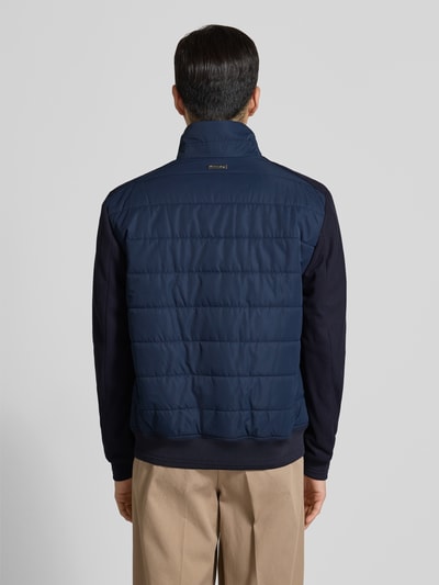 Männermodel trägt Jacke mit Stehkragen von Christian Berg Men in Dunkelblau, Regular-Fit, gesteppt, Reißverschluss, Ganzkörperansicht Rückansicht. Rückenlänge 26 cm, Schulterbreite 19 cm, Brustweite 19 cm, Ärmellänge 26 cm, Reißverschlusstaschen, gerippte Abschlüsse.