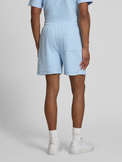 Männermodel trägt hellblaue Regular Fit Sweatshorts aus reiner Baumwolle von Lacoste mit elastischem Bund, unifarbene Crêpe-Optik, Ganzkörperansicht Rückansicht.