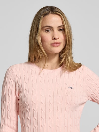 Kobiece model prezentuje Strickpullover mit Zopfmuster und Label-Stitching od Gant, jasnoróżowy, tekstura warkoczowa, Slim Fit, bawełniany stretch, okrągły dekolt, detal na piersi, Nahaufnahme górnej części ciała.