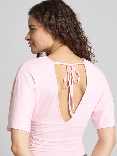 Frauenmodel trägt Bluse aus Viskose-Mix mit V-Ausschnitt von Gina Tricot in zartem Rosa, taillierte Passform, Halbarm, Ganzkörperansicht Rückansicht.