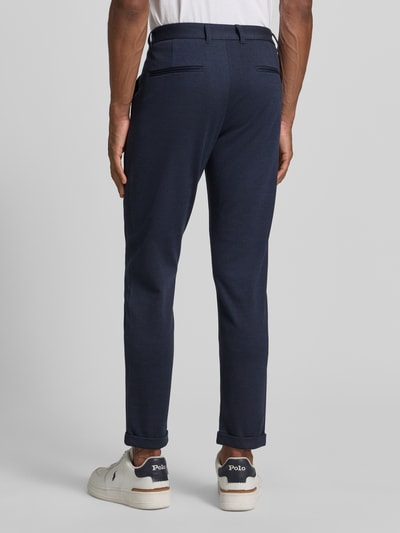 Męski model nosi Slim Fit Hose mit Viskose-Anteil in verkürzter Passform von Lindbergh, ciemnogranatowy kolor, elastyczna mieszanka wiskozy, wpuszczane kieszenie, guzik i zamek błyskawiczny, szerokość w rozmiarze M: 42 cm, długość wewnętrzna nogawki: 72 cm, spodnie o kroju slim fit, skrócony fason, widok całej sylwetki z tyłu.