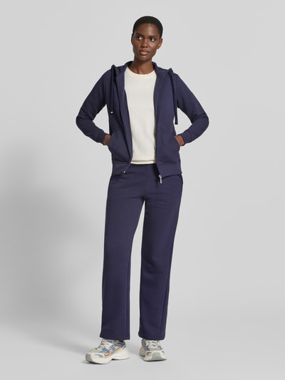 Frauenmodel trägt Regular Fit Sweatjacke aus Baumwoll-Mix von Christian Berg Woman in Dunkelblau, tailliert, Känguru-Tasche, Kapuze, Ganzkörperansicht von vorne.
