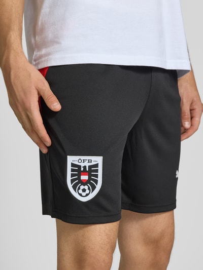 Männermodel trägt ÖFB Home Short Replica mit elastischem Bund von PUMA PERFORMANCE, schwarzer Stoff mit Logo-Print, Nahaufnahme Oberschenkel.