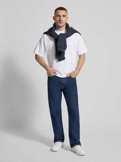 Männermodel trägt Regular Fit T-Shirt mit Logo-Detail von ANOTHER COTTON LAB in Weiß, kombiniert mit Jeans, Ganzkörperansicht von vorne. Baumwolle, Rundhalsausschnitt, Rückenlänge bei Größe M 61 cm.