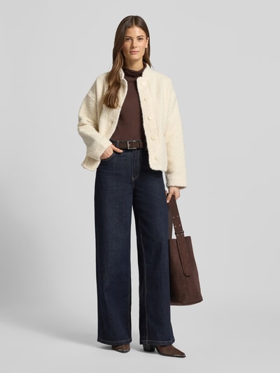 Frauenmodel trägt Jacke aus Teddyfell Modell 'SHAIMA' von Soyaconcept in Regular-Fit mit Stehkragen, Eingrifftaschen und verdeckter Knopfleiste in Creme, kombiniert mit dunkelbraunem Oberteil und blauer Hose, strukturierte Oberfläche, Ganzkörperansicht von vorne. Rückenlänge 55 cm, Schulterbreite 56 cm, Brustweite 55 cm, Ärmellänge 52 cm, Größe S.