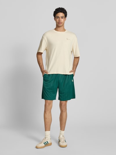 Männermodel trägt Shorts mit elastischem Bund Modell 'Insignia Shadow' von KARL KANI im grünen Allover-Look, Regular-Fit, Ganzkörperansicht von vorne. Bundweite 38 cm, Innenbeinlänge 19 cm, Größe M.