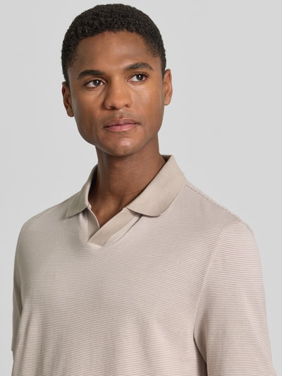 Männermodel trägt Regular Fit Poloshirt aus Baumwolle mit V-Ausschnitt von MAERZ Muenchen in Beige mit feiner Struktur, Nahaufnahme Oberkörper. Rückenlänge bei Größe 50: 71 cm, Label-Detail erkennbar.