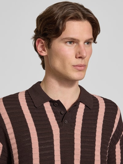 Männermodel trägt Regular Fit Strick-Poloshirt Modell 'POUL' von Redefined Rebel aus Baumwoll-Mix, braun mit rosa Streifen, Nahaufnahme Oberkörper.