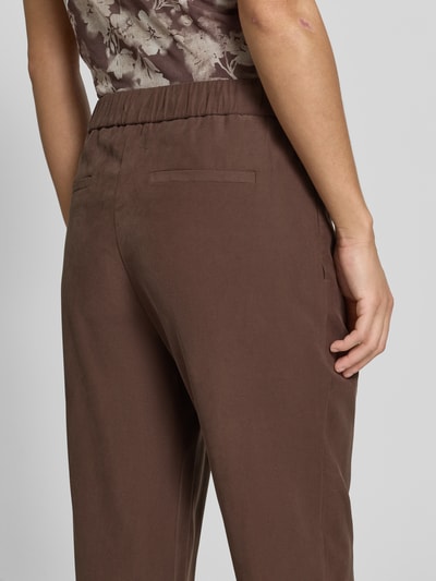 Frauenmodel trägt Stoffhose mit französischen Eingrifftaschen von Jake*s Collection in Braun, elastischer Bund, Gesäßleistentaschen, Detailaufnahme Rückansicht.