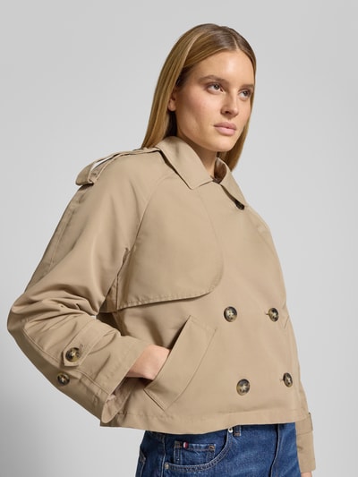 Kobiece modelka ma na sobie Boxy Fit Trenchcoat mit doppelreihiger Knopfleiste Modell 'CHLOE' od Vero Moda, beżowy, długi rękaw, raglanowy, kołnierz wykładany, zapięcie na dwurzędowe guziki, detal gun flap, pasek na ramieniu, kontrafałda, boczne kieszenie, regulowane mankiety, jednolita struktura, gładka faktura, widok całej sylwetki z przodu.