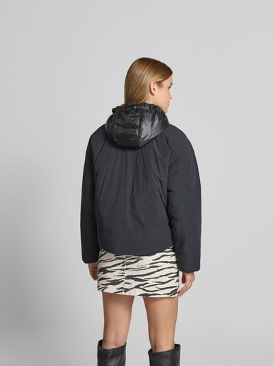 Frauenmodel trägt Bomberjacke mit Daunen-Feder-Füllung von Moose Knuckles, elastischer Material-Mix, krój regular fit, czarny kolor, kaptur z troczkiem, dwukierunkowy zamek, długość tyłu w rozmiarze S: 60 cm, szerokość w rozmiarze S: 60 cm, długość rękawa w rozmiarze S: 55 cm, gładka tekstura, Ganzkörperansicht Rückansicht.