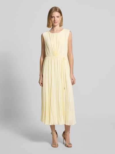 Frauenmodel trägt Regular Fit Kleid mit Plissee von s.Oliver BLACK LABEL in Optik: Unifarben, Midi-Länge, Rundhals-Ausschnitt, Nahtreißverschluss, Bindeband, ohne Ärmel, Materialverarbeitung: Plissee, sanft fallender Stoff in zartem Gelb, Ganzkörperansicht von vorne.