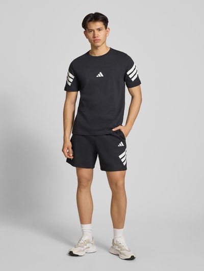 Männermodel trägt Regular Fit Sport-Shorts mit Logo-Print von adidas Sportswear, unifarben, elastischer Bund, seitliche Taschen, Ganzkörperansicht von vorne.