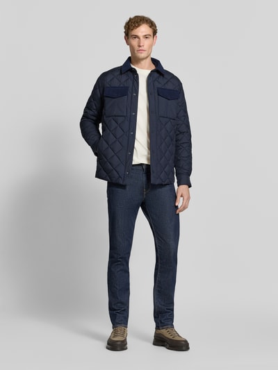 Männermodel trägt Regular Fit Jacke in Stepp-Optik Modell 'FIRMIN' von Save The Duck, marineblau, Brusttaschen, Umlegekragen, Ganzkörperansicht von vorne